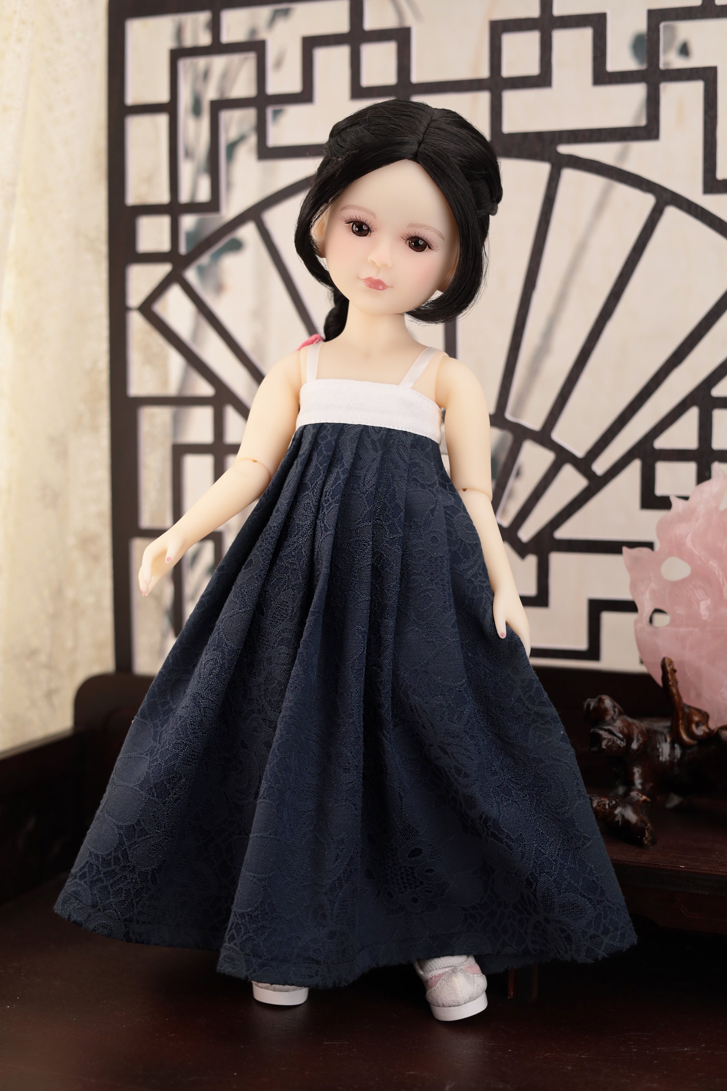 Doll wearing a dark blue dress with a white top against a decorative wall.