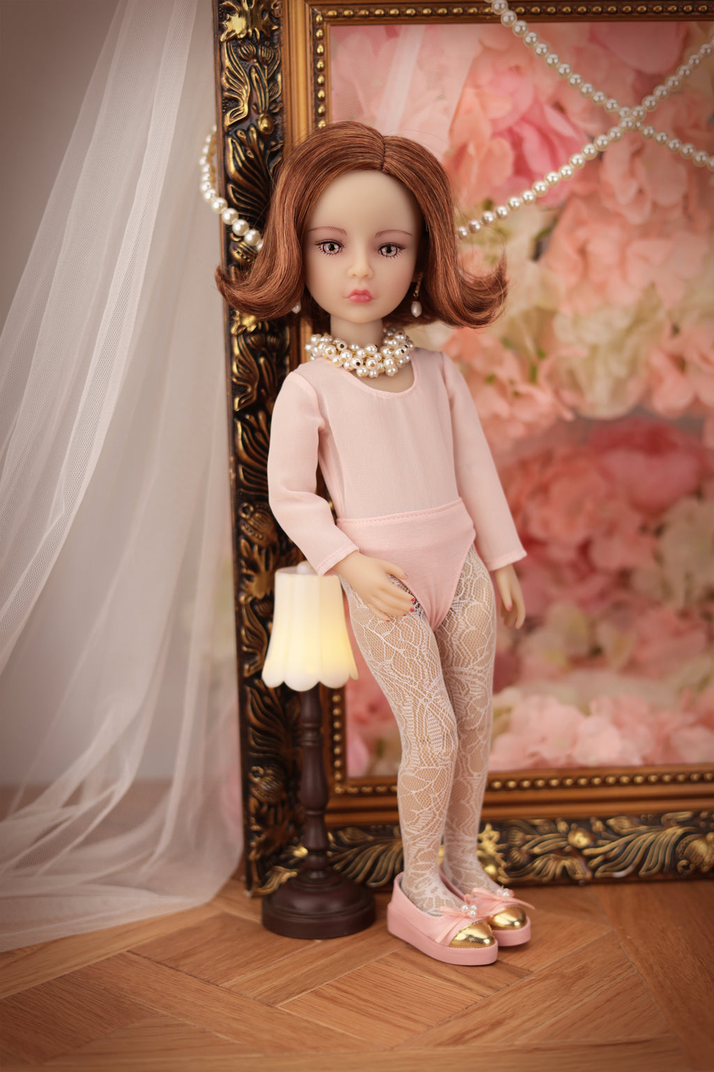 Lou in a pink outfit standing next to a decorative lamp with a floral background