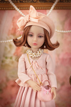 Lou in a pink dress and hat with a pearl necklace and handbag against a blurred floral background