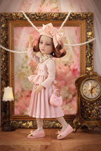 Lou in a pink dress with a matching handbag standing in front of an ornate frame and clock.