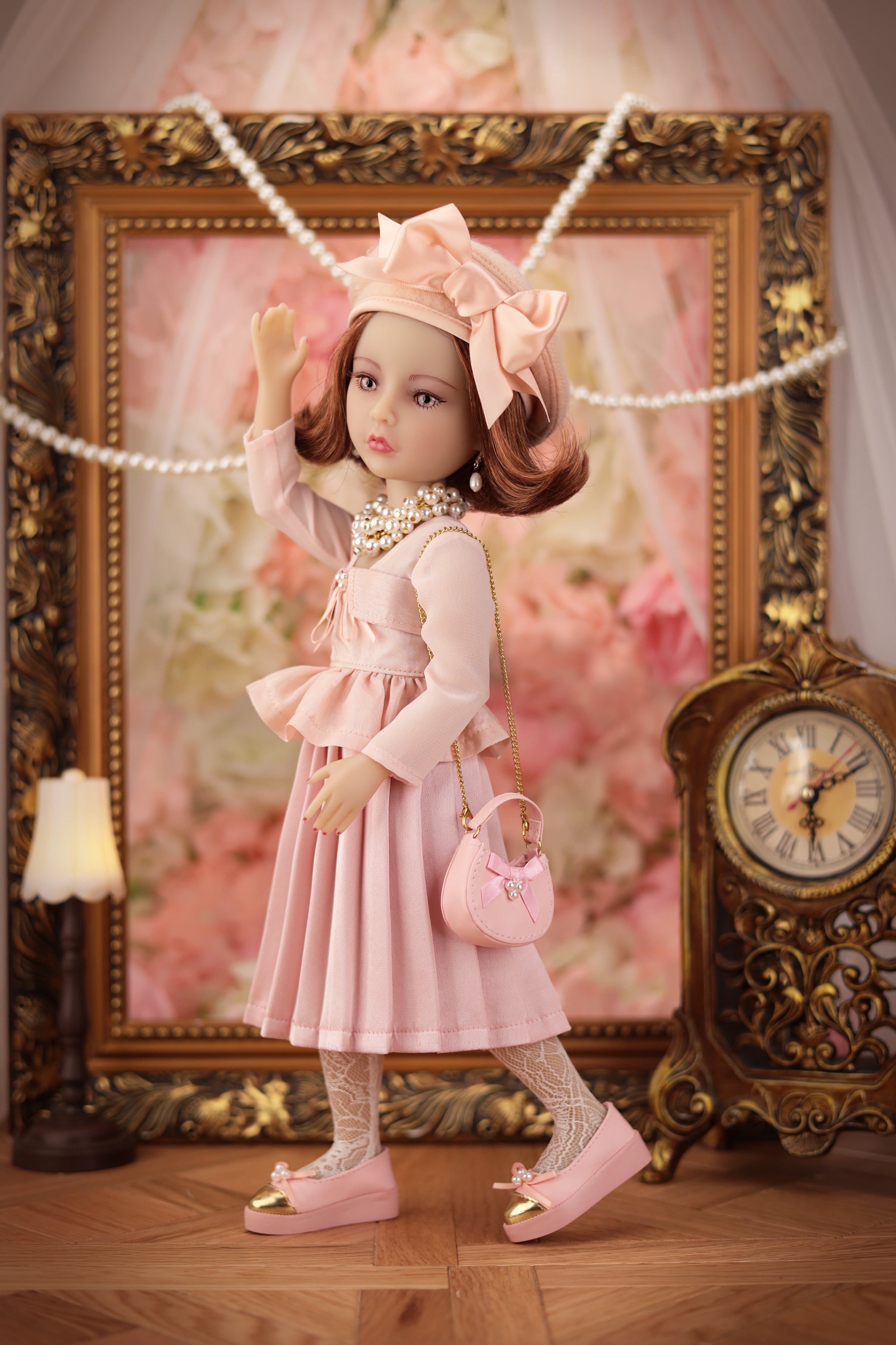 Lou in a pink dress with a matching handbag standing in front of an ornate frame and clock.
