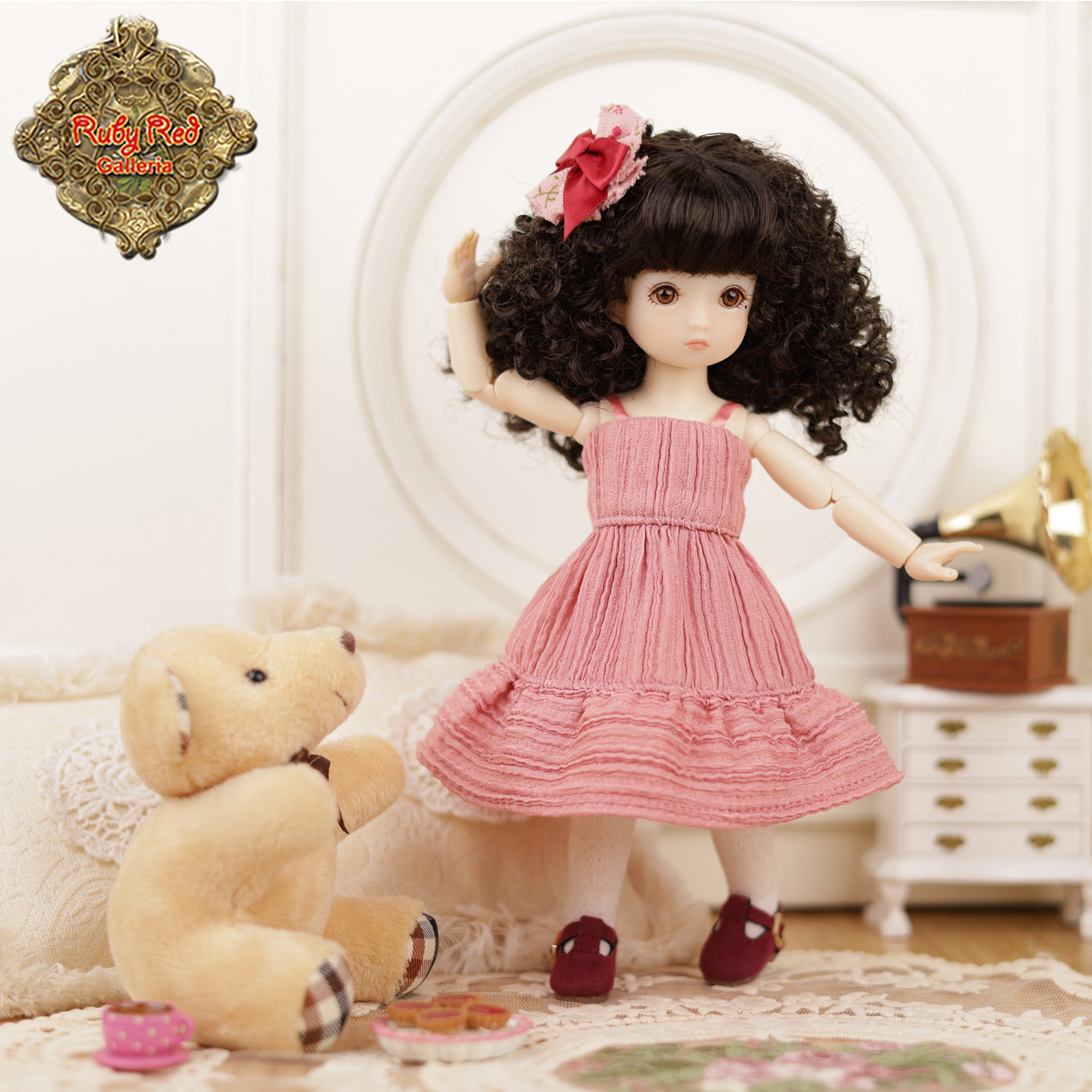 Doll in a pink dress with curly hair and a teddy bear in a room setting.