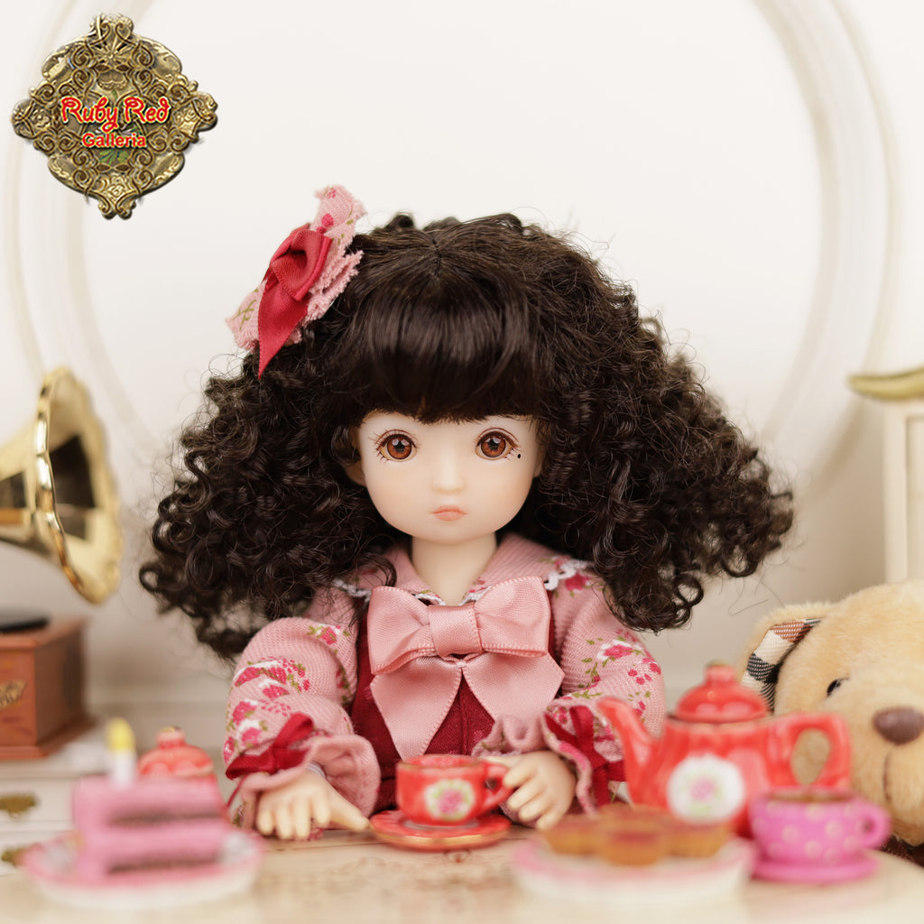 Doll with curly hair and floral headband sitting at a tea set with 'Ruby Red Dolls' logo.