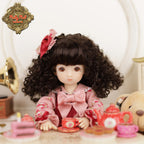 Doll with curly hair and floral headband sitting at a tea set with 'Ruby Red Dolls' logo.