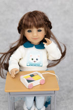 8" mini Fashion Friends Doll with a white sweater featuring a cat design, sitting at a small table with a colorful toy.