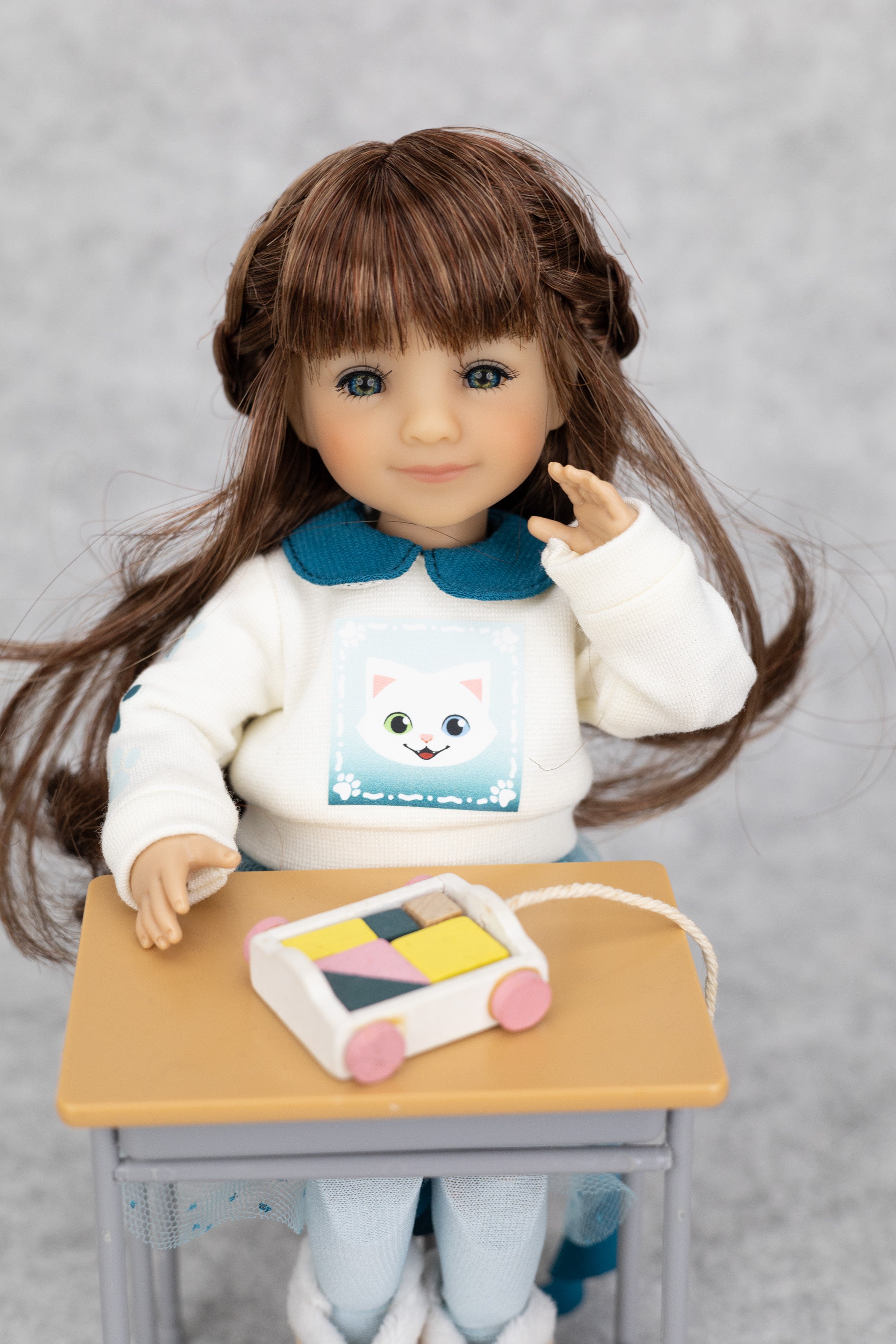 8" mini Fashion Friends Doll with a white sweater featuring a cat design, sitting at a small table with a colorful toy.
