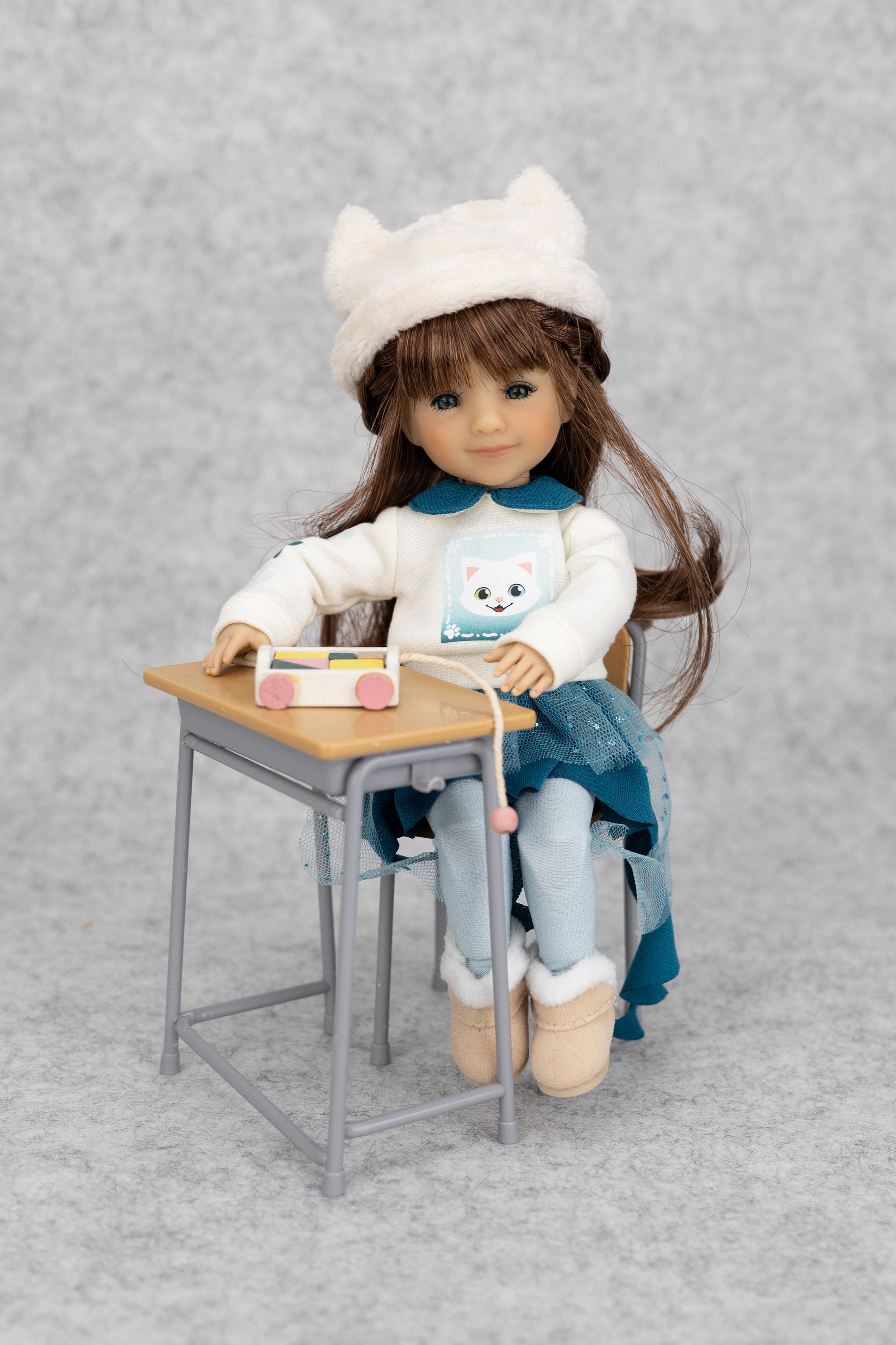 8" mini Fashion Friends Doll sitting at a small desk with a gray background