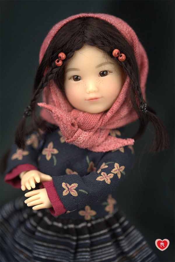 Doll wearing a pink scarf and dark floral dress against a dark background