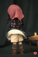 Back view of a doll wearing a pink headscraft, floral-patterned coat, and boots on a dark background.