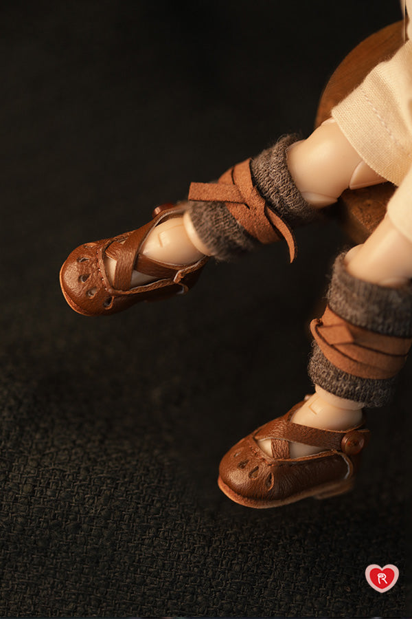 Close-up of doll feet wearing brown sandals and brown socks on a dark background