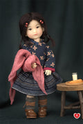 Doll with dark hair and floral-patterned outfit holding a pink scarf, standing next to a small wooden stool with a glass and bread.