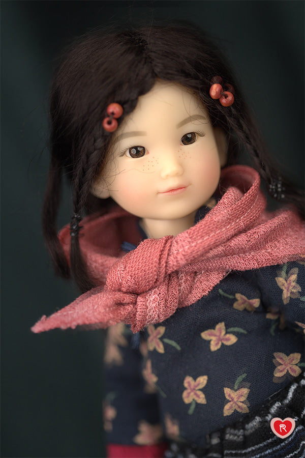 Close-up of a doll with a pink scarf and floral patterned outfit against a dark background