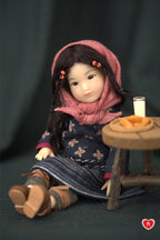 Doll wearing a pink hood and floral dress sitting next to a small table on a dark background