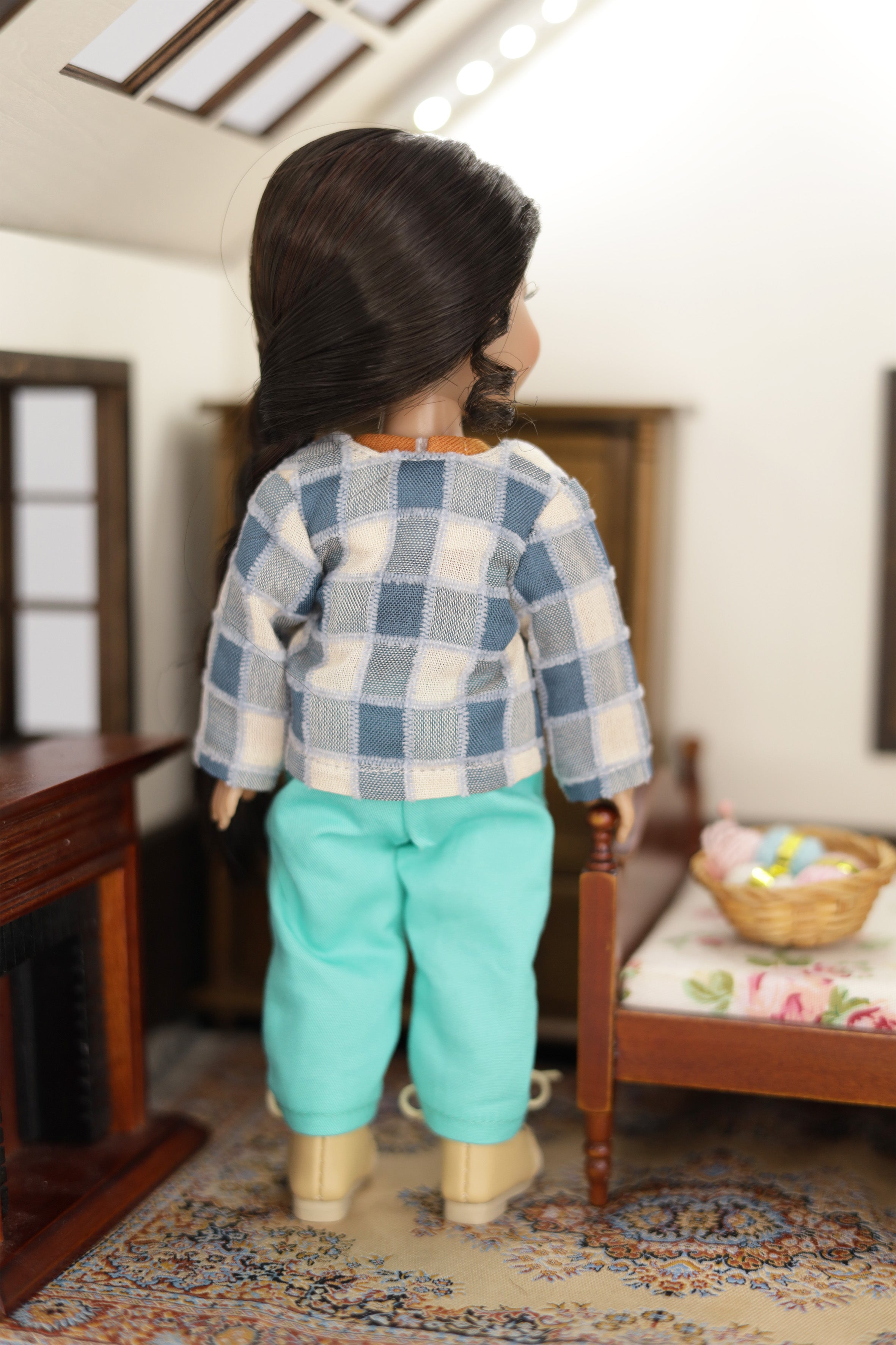 mini Freida doll wearing a plaid shirt and turquoise pants standing in a room with furniture and decor.