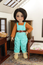 mini Freida doll wearing a turquoise jumpsuit and brown shirt in a room setting.