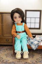 mini Freida wearing a turquoise jumpsuit with a brown belt, sitting on a bed in a room.