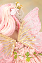 A close-up of a pink fairy costume accessory set, featuring sheer pink wings with gold trim, a pink ruffled dress, and pink hair with small white flowers.