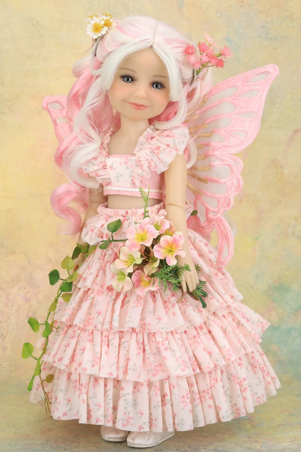 A doll  of a fairy girl with long white and pink hair, pink wings, and a pink floral dress, holding a bouquet of flowers against a soft pastel background.