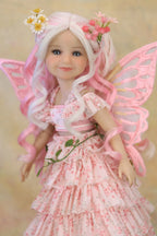 A doll with long wavy white and pink hair, wearing a pink floral fairy dress and translucent pink wings, posed against a soft beige background.