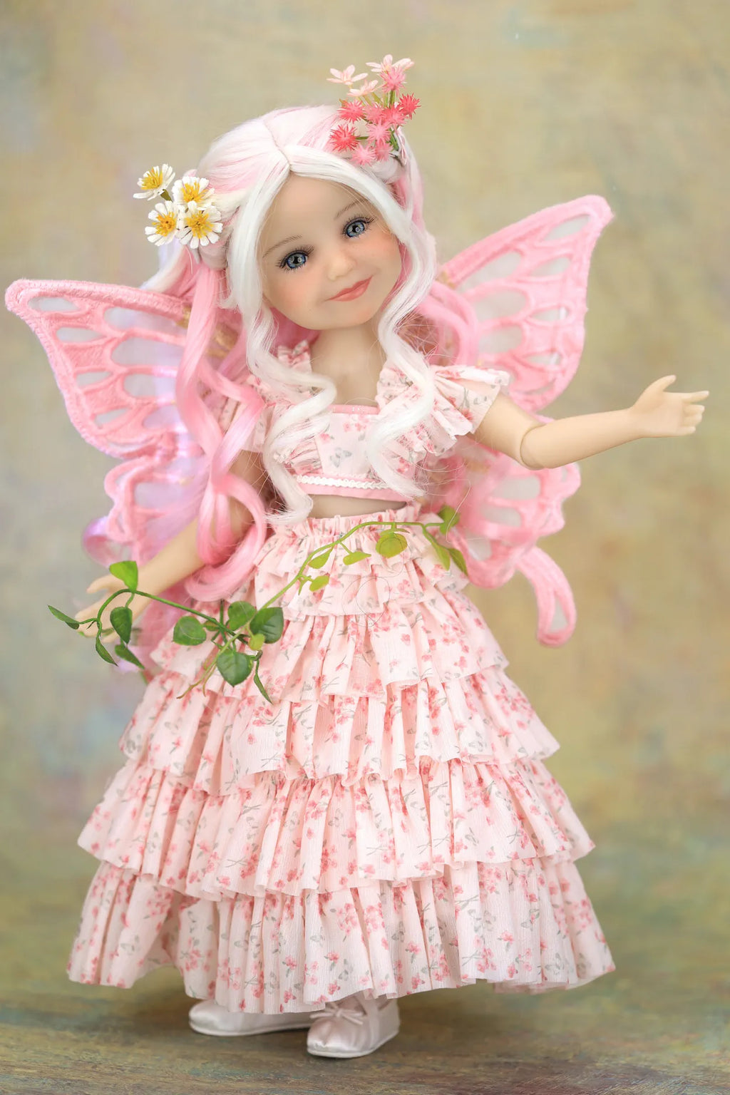A fairy-themed doll with long white hair, pink wings, and a pink floral tiered dress, posed against a soft beige background.