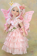 A fairy doll with long white hair, pink wings, and a pink floral dress, posed against a soft beige background.