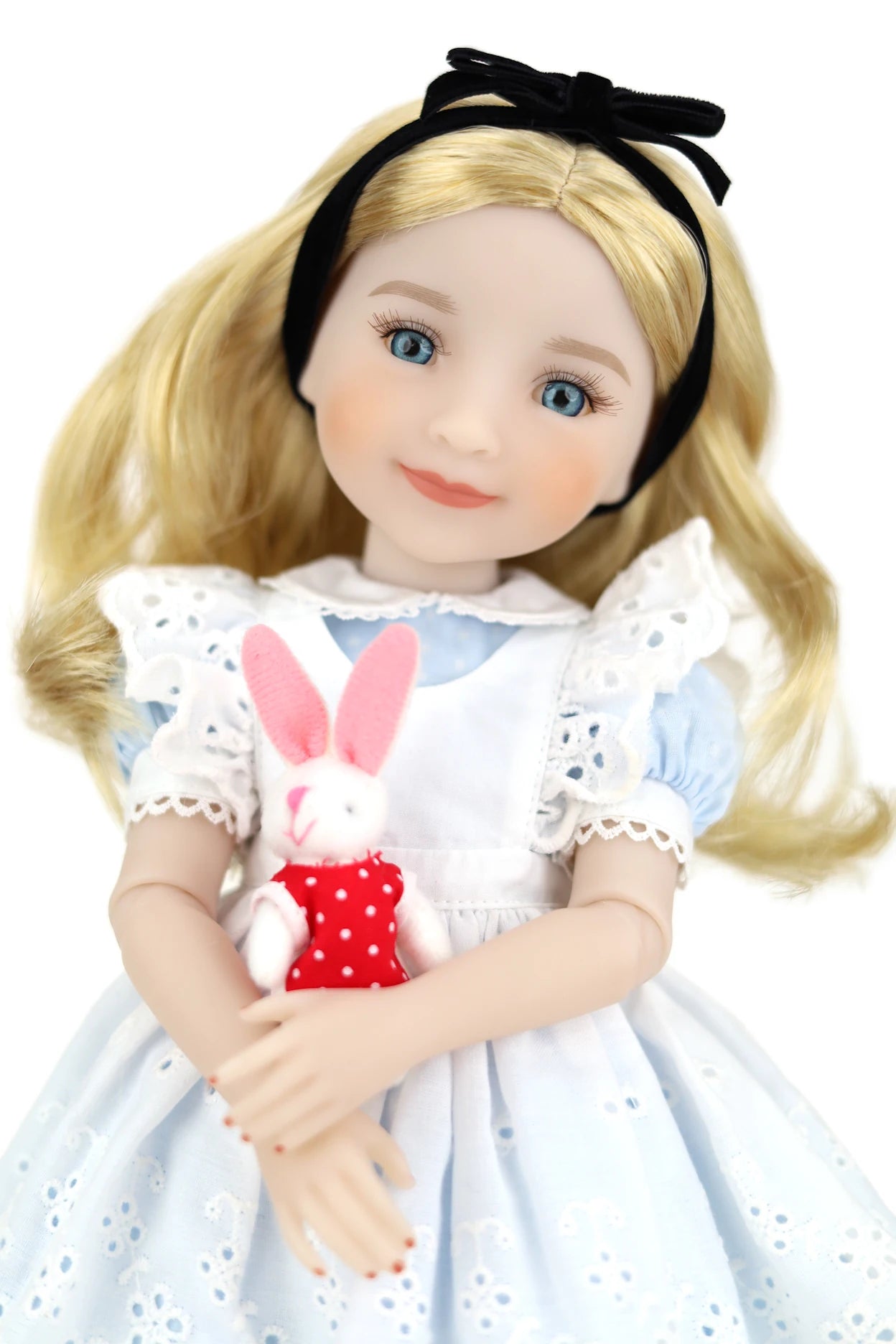 Doll in Alice in Wonderland outfit holding a rabbit plush toy on a white background