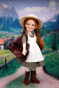 Doll with red hair and a white dress standing in a scenic outdoor setting with mountains and a village.
