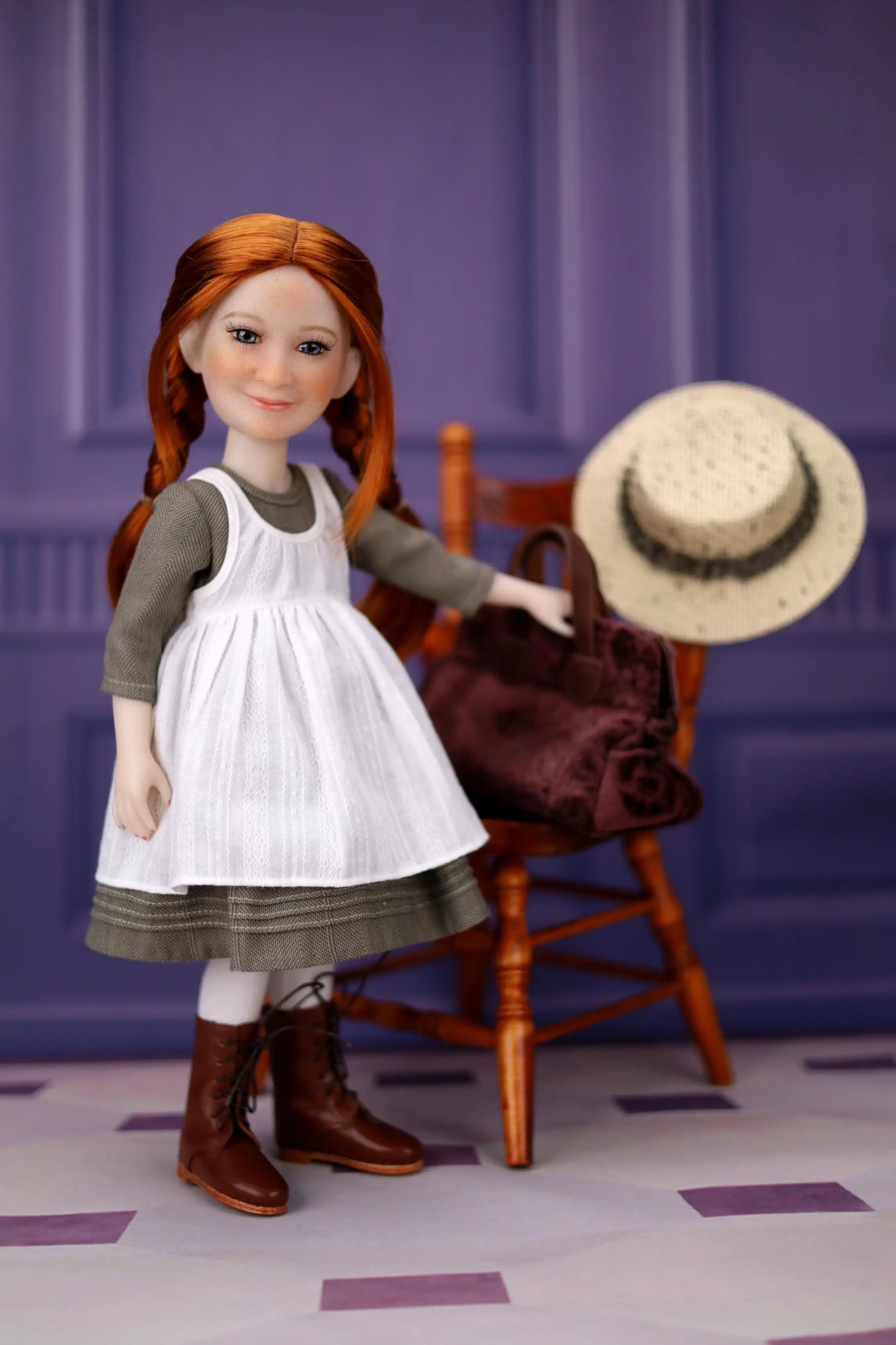Doll with red hair wearing a white dress and brown boots, standing next to a wooden chair and straw hat against a purple wall.