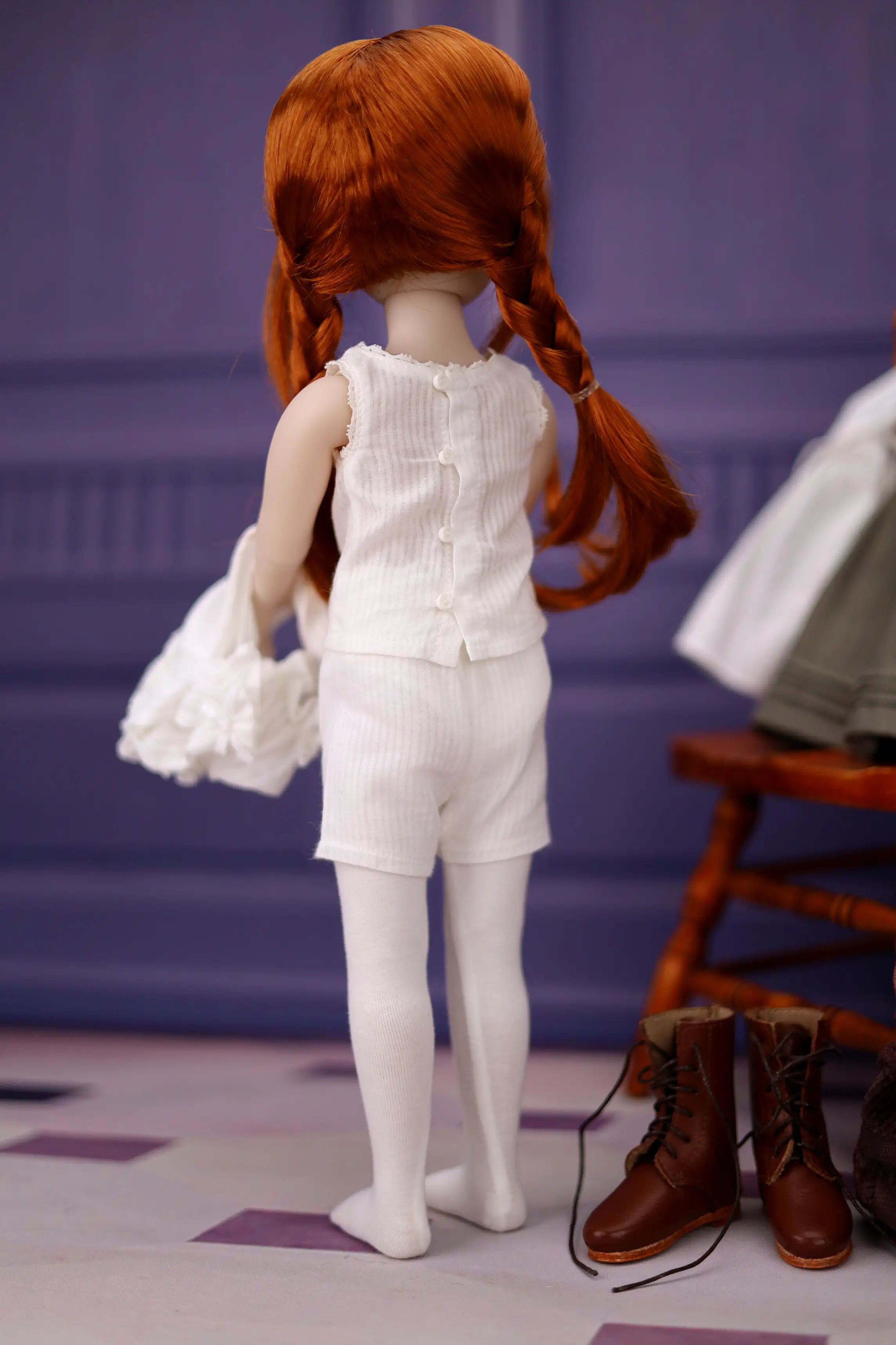 Doll with red hair styled in pigtails, wearing a white outfit, standing on a checkered floor.