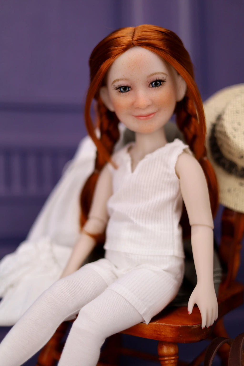 Doll with red hair wearing a white outfit sitting on a wooden chair against a purple background