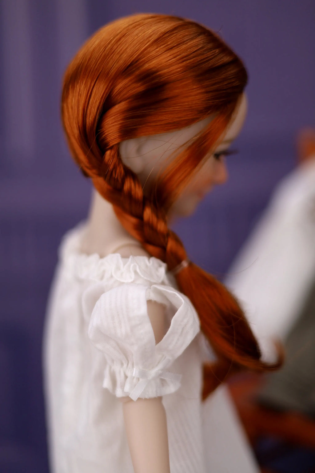 Doll with red hair styled in a braid, wearing a white dress against a purple background