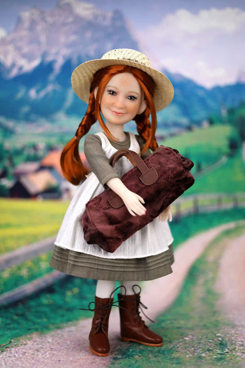 Doll with red hair and a straw hat standing on a path with mountains in the background