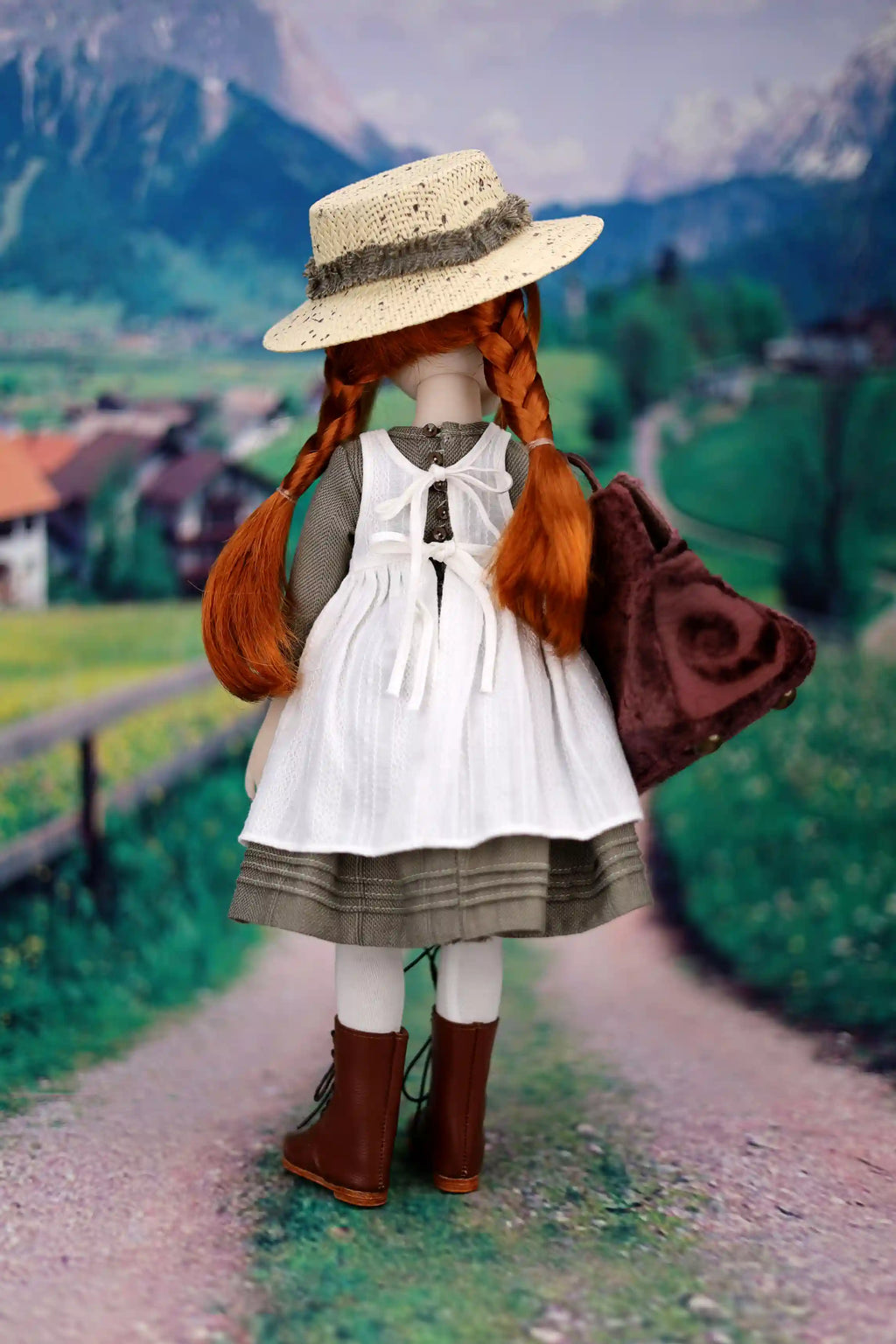 Vintage-style doll with red hair and a straw hat standing on a path with mountains in the background