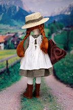 Vintage-style doll with red hair and a straw hat standing on a path with mountains in the background