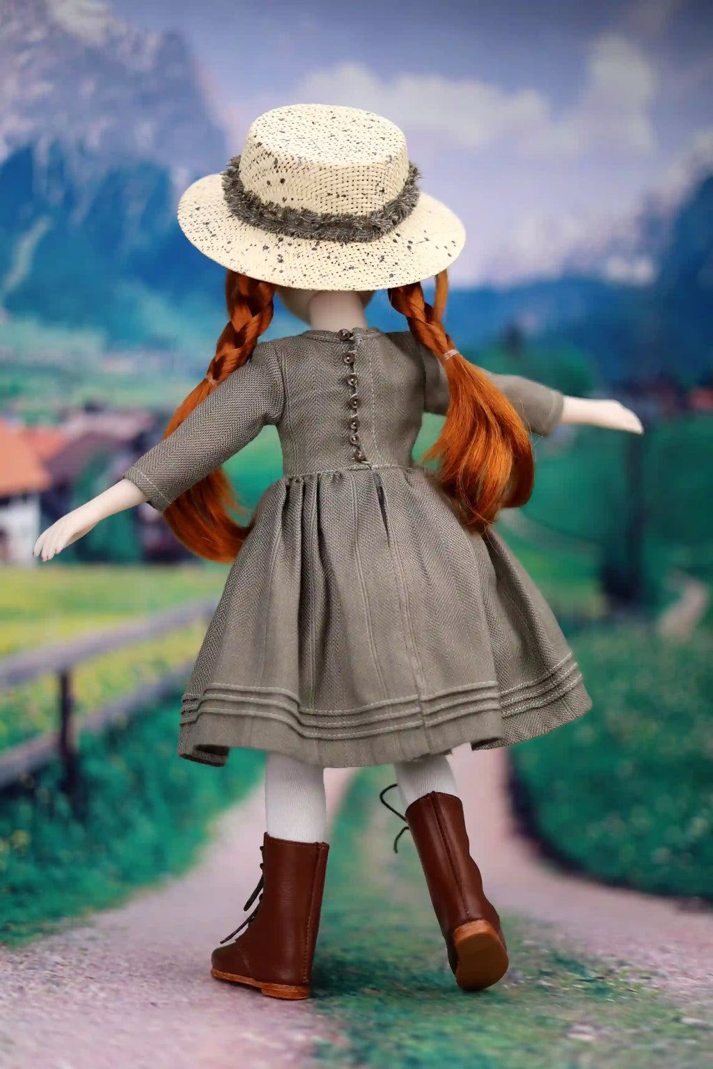 Doll with red hair and a gray dress standing on a path with a scenic background
