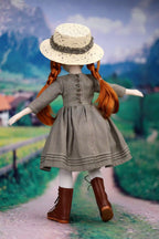 Doll with red hair and a gray dress standing on a path with a scenic background