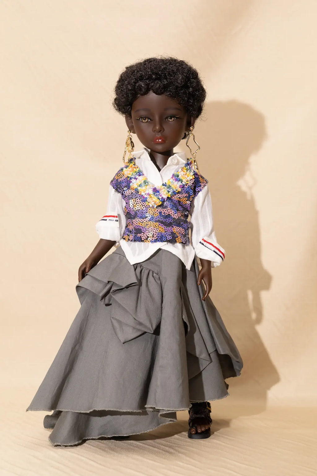 Doll wearing a floral vest, white shirt, and gray skirt against a beige background