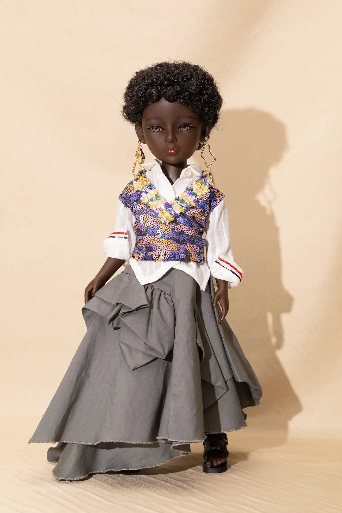 Doll wearing a floral vest, white shirt, and gray skirt against a beige background