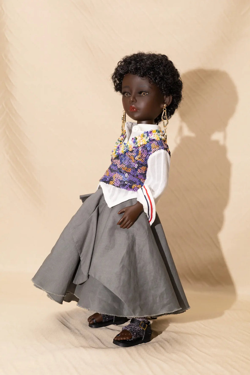 Doll wearing a floral vest, white shirt, gray skirt, and shoes on a beige background