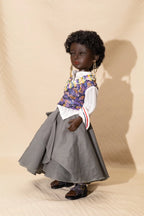 Doll wearing a floral vest, white shirt, gray skirt, and shoes on a beige background