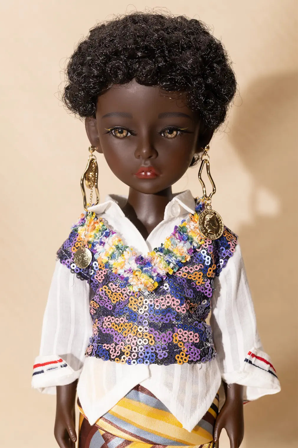Doll wearing a colorful sequined vest over a white shirt on a beige background