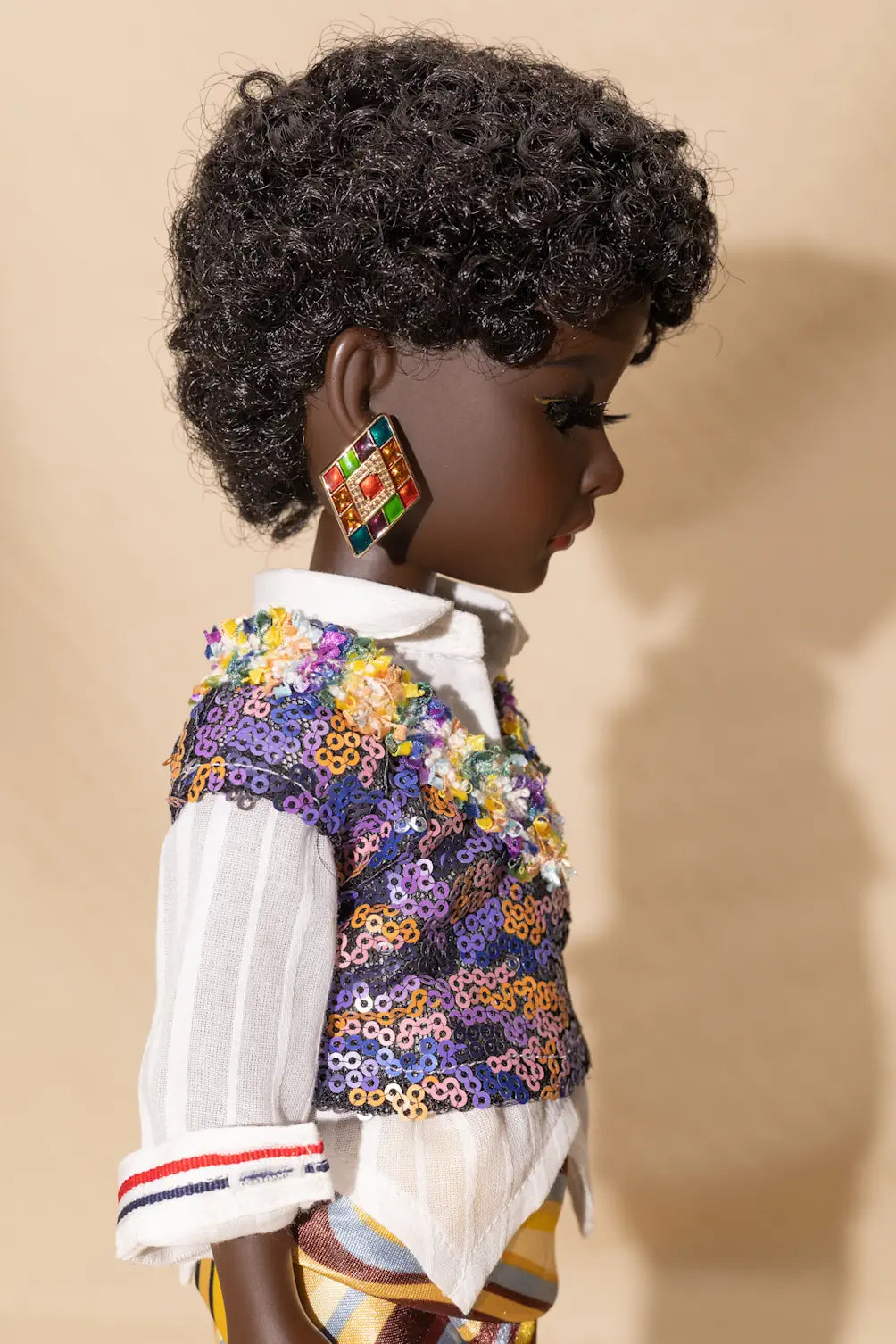 Doll wearing a colorful jacket and patterned earrings against a beige background