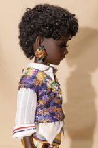 Doll wearing a colorful jacket and patterned earrings against a beige background