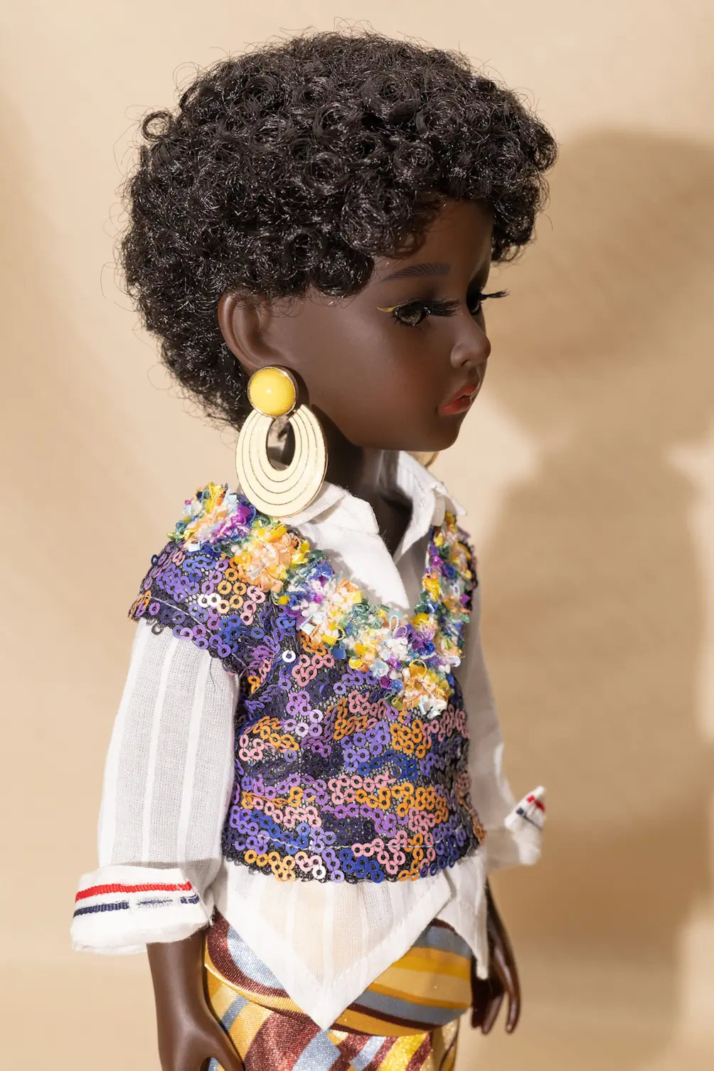 Doll wearing a colorful floral vest over a white shirt on a beige background