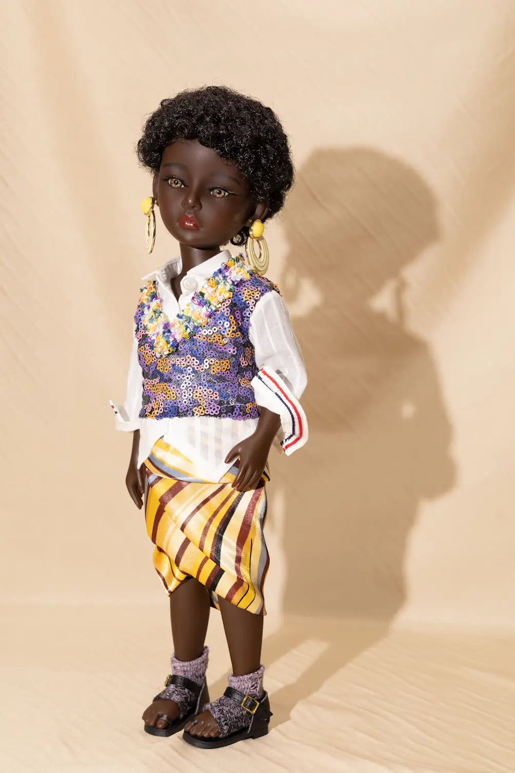 Doll wearing a colorful outfit with a vest and striped skirt on a beige background