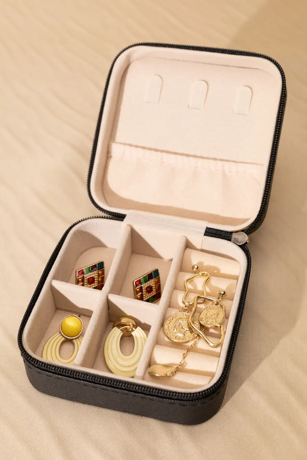 Open jewelry case with gold earrings on a beige background