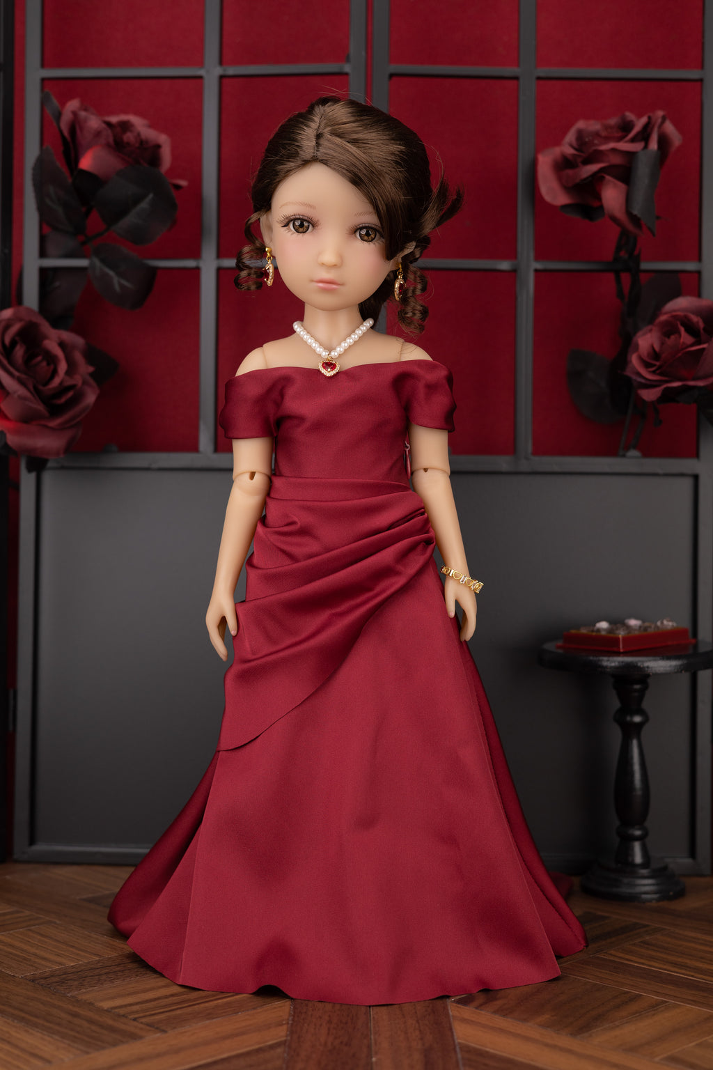 Doll in a red off-shoulder dress against a decorative wall with roses.
