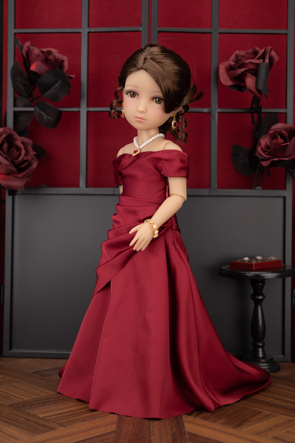 Doll in a red dress standing against a decorative wall with roses.