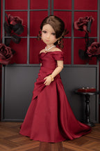 Doll in a red dress standing against a decorative wall with roses.