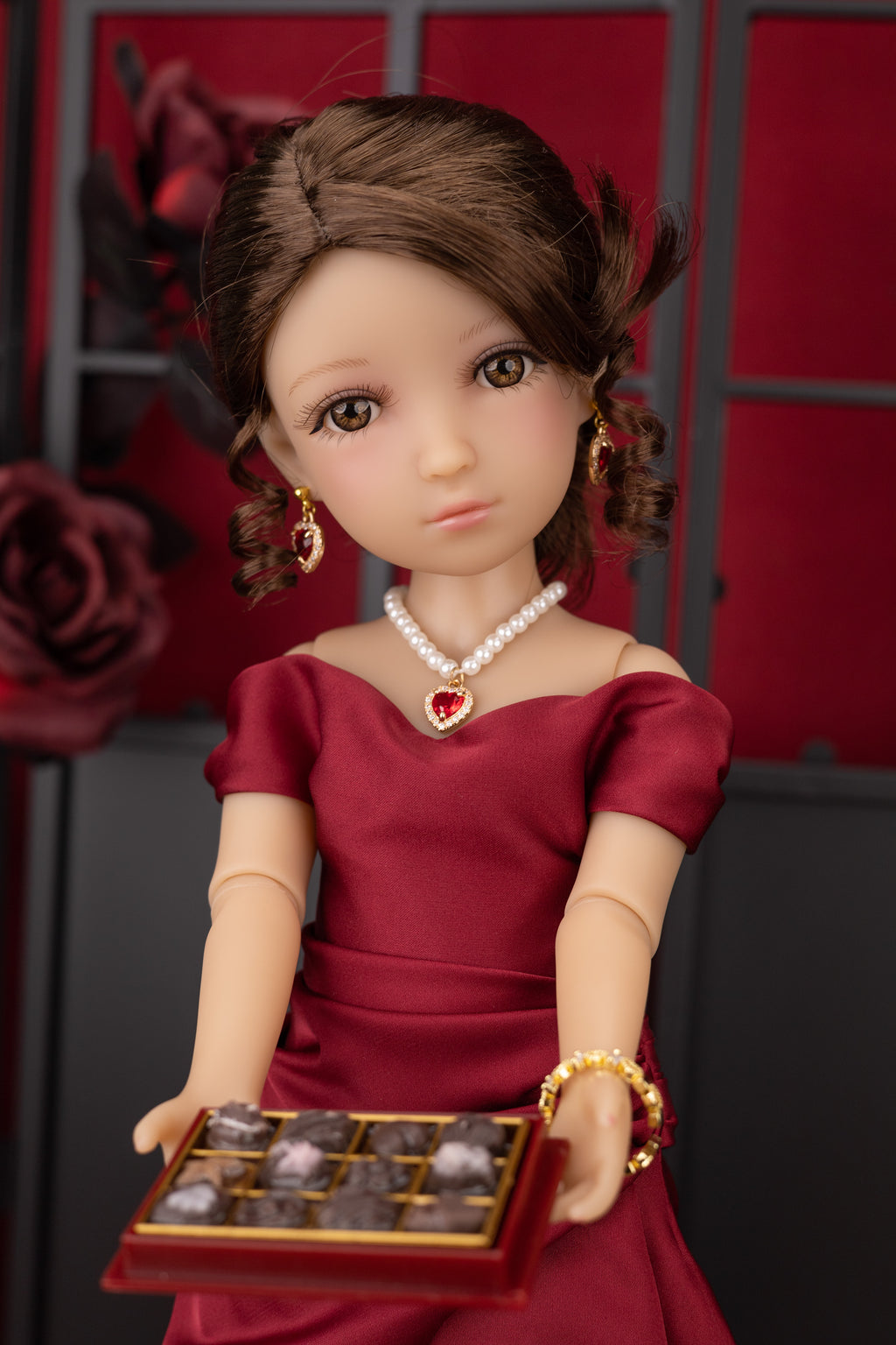 Doll in a red dress holding a tray of chocolates against a red and black background
